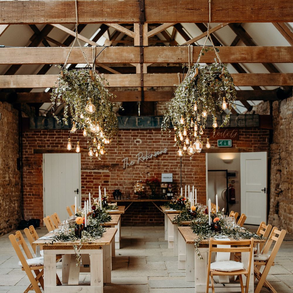Barn reception venue with wooden tables, hanging ivy and lights
