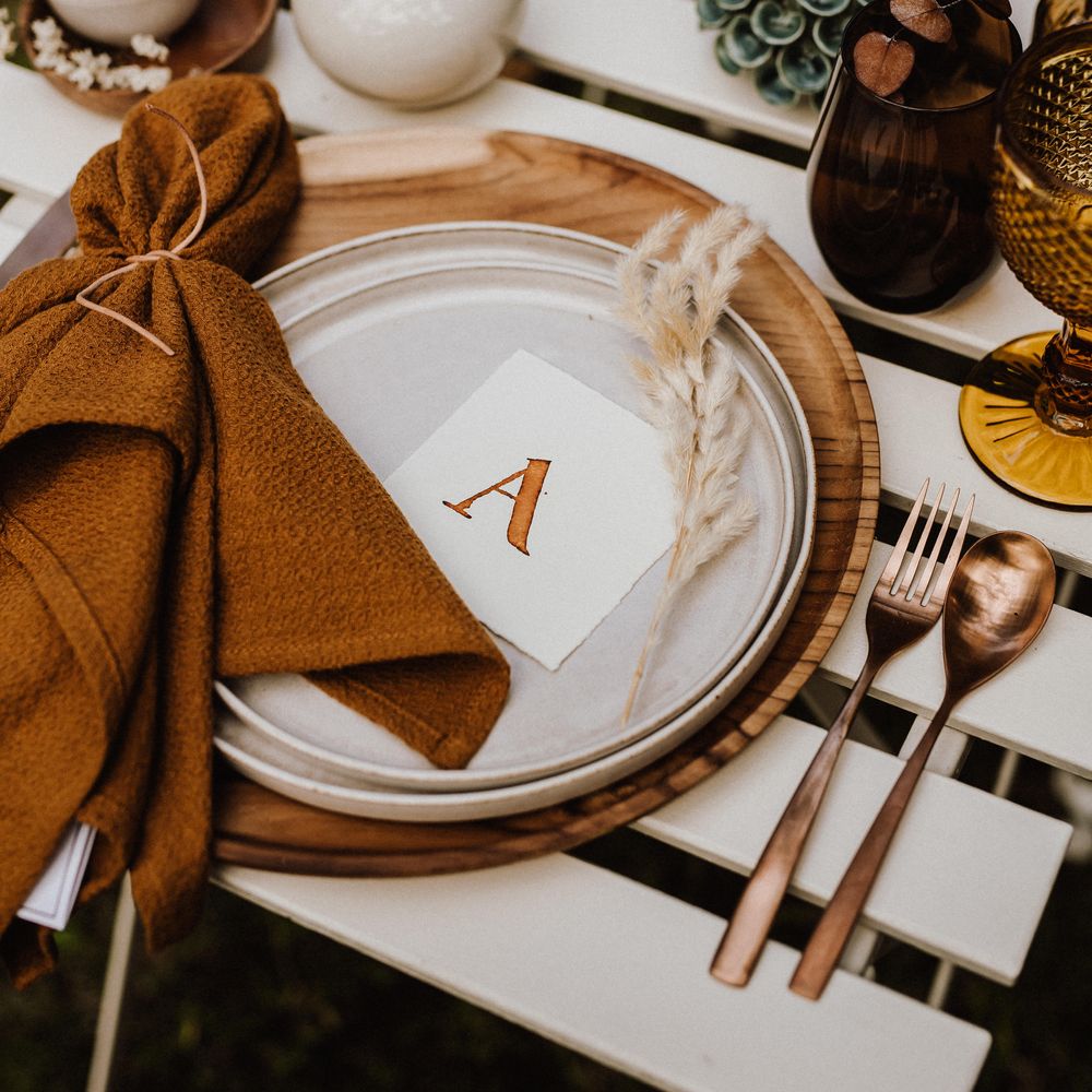 White plate with burnt orange napkin and sprig of pampas grass