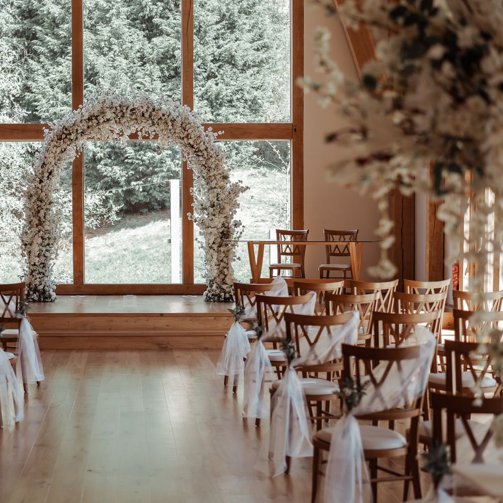 Wedding aisle lined with chairs and floral archway sits to the front of the room