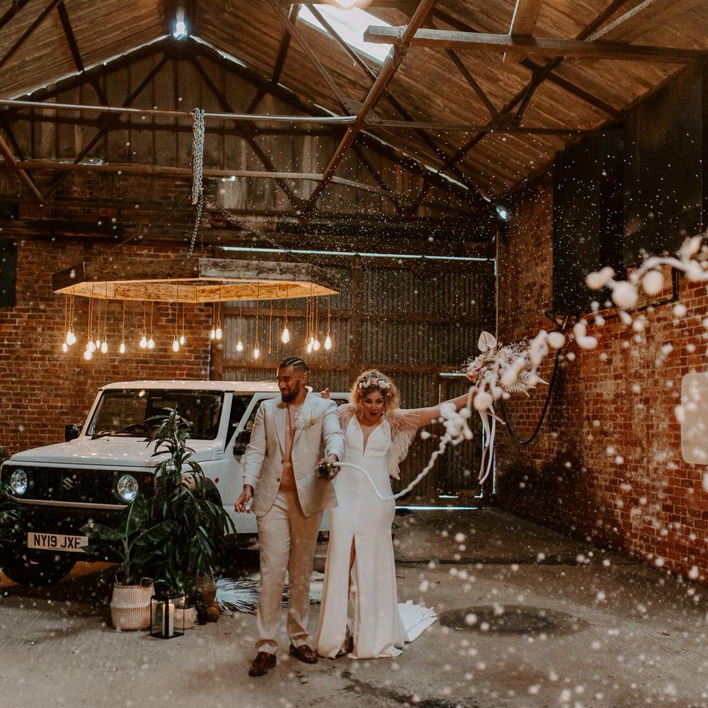 Bride and groom spraying champagne in a warehouse next to a large white 4x4 jeep with plants