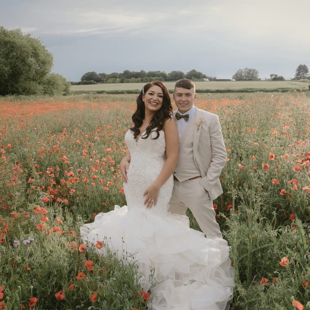 Bride and groom portrait in a poppy field with the bride in a Mori Lee mermaid wedding dress and groom in a three piece beige suit