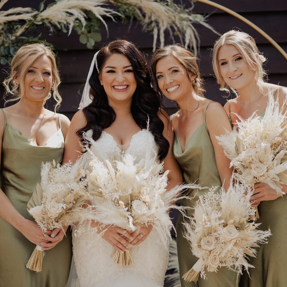 Bridal party portrait with bride in a lace fitted wedding dress and bridesmaids in green sating midi dresses 