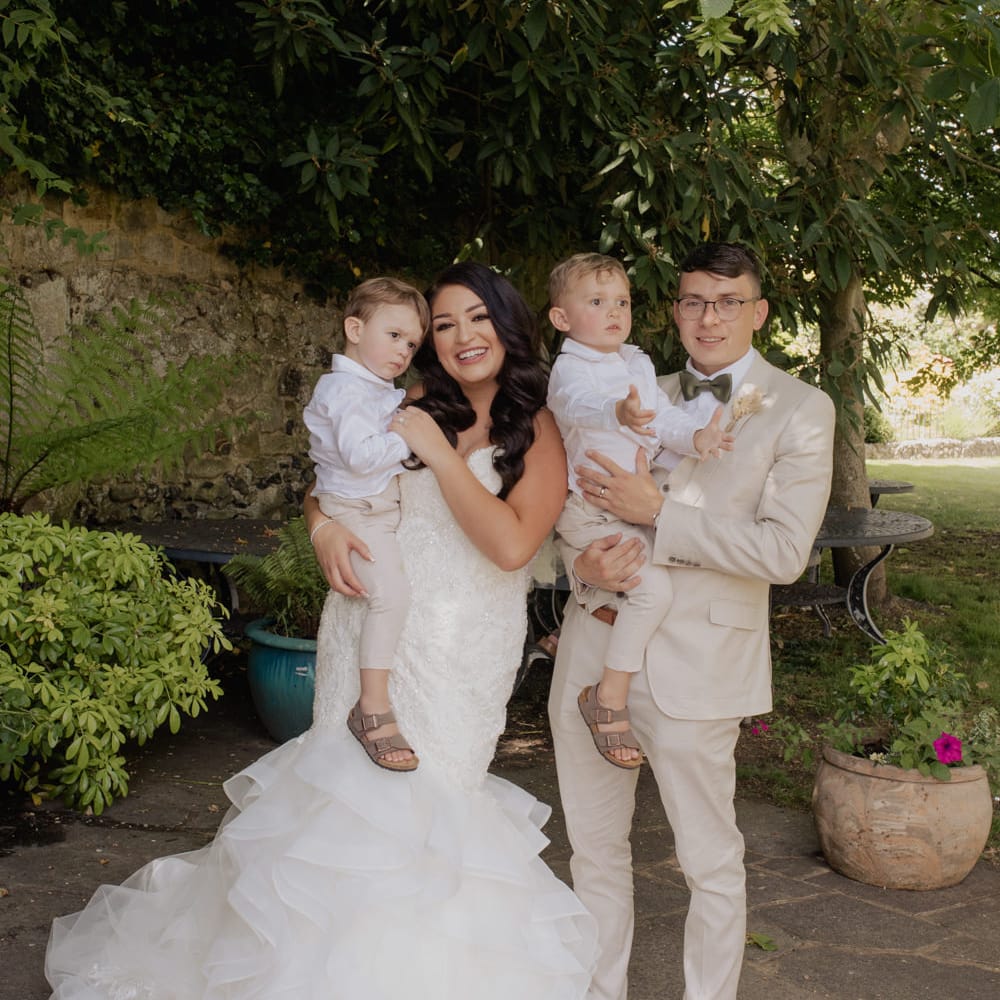 Bride and groom fairy portrait with their two boys. The bride wears a fishtail wedding dress and the groom and page boys beige suits 