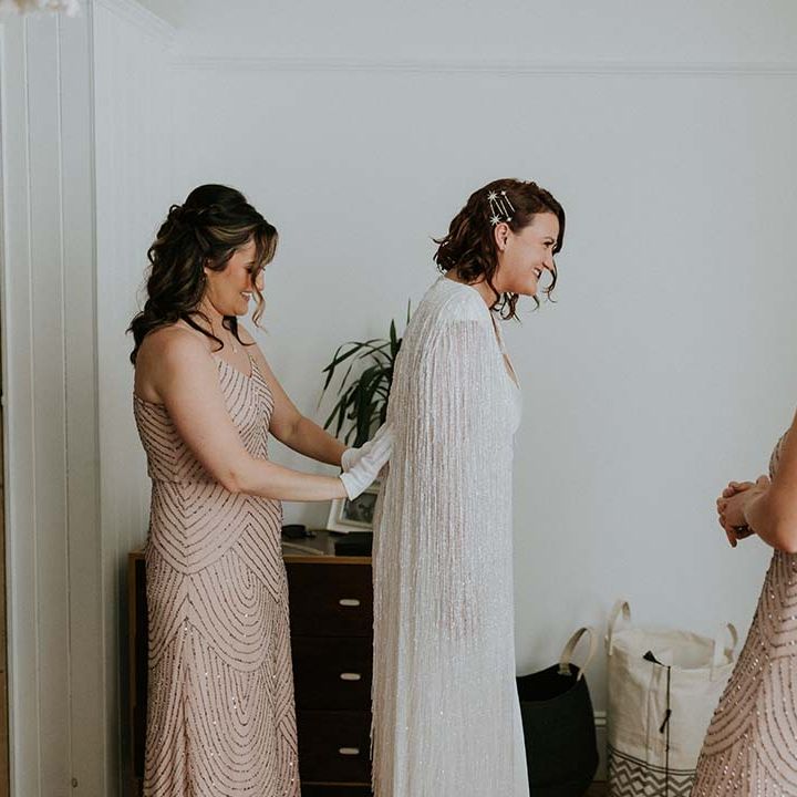 Bridesmaid does up brides wedding cape on the day of her wedding