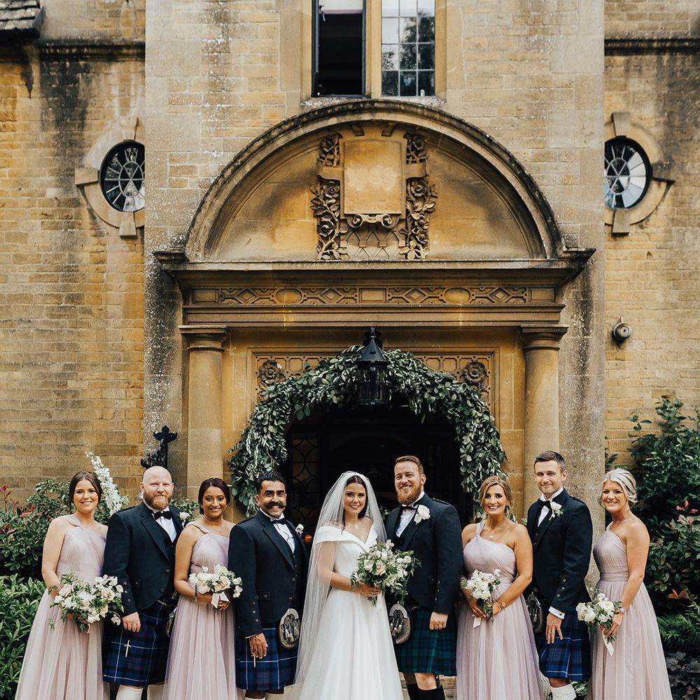 Wedding party portrait with bridesmaids in pale pink dresses, and groomsmen in tartan kilts at Foxhill Manor with foliage arch decor 