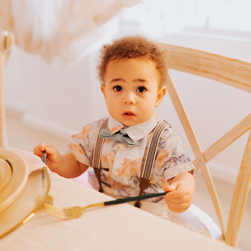Page boy in a patterned shirt with bow tie and braces sitting at the top table with gold cutlery 