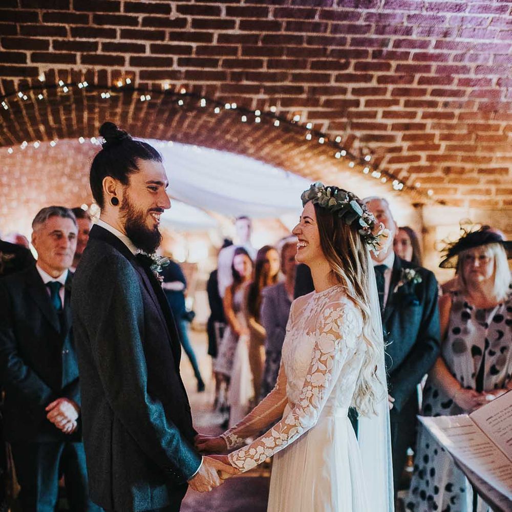 Bride in a lace long sleeve wedding dress and flower crown smiling holding hands with her groom during the civil wedding ceremony