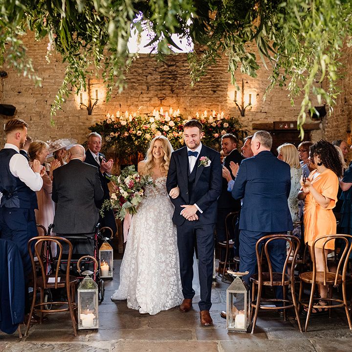 Bride and groom walk out of their ceremony as a married couple with lots of greenery decor 