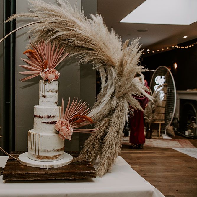 Three tier naked wedding cake featuring white frosting and complete with pink pastel decor and florals 