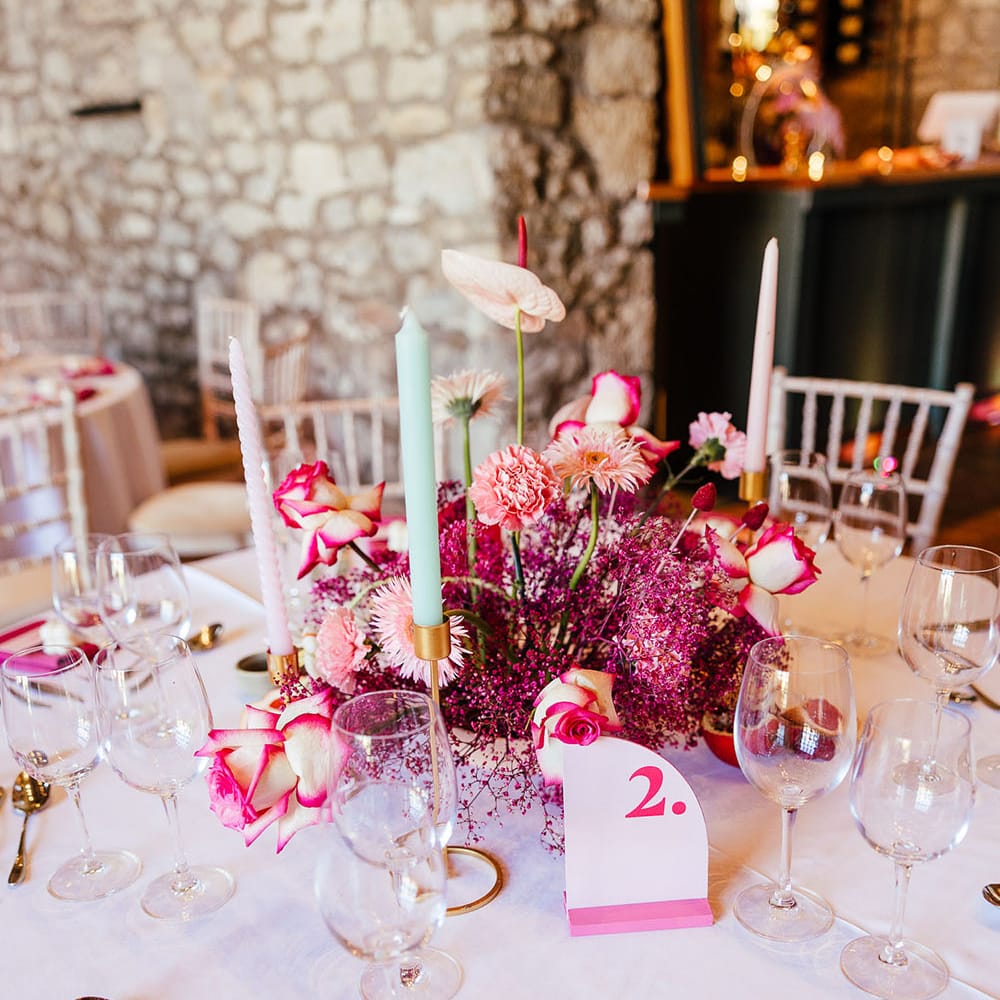 Bright pink floral centrepiece for modern tablescape complete with pink table numbers and pastel candles in gold candle holders 
