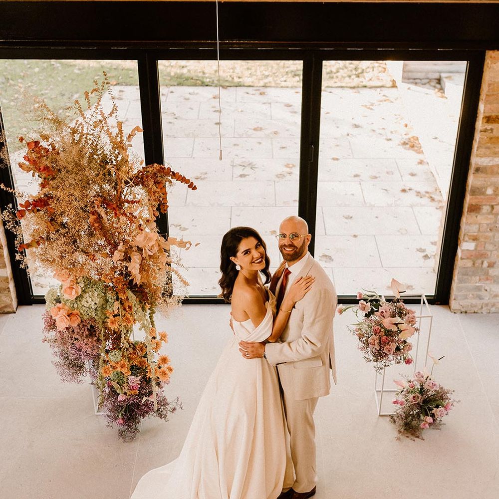 Bride and groom embrace at the altar looking up at the camera with the rust and lavender wedding flowers 