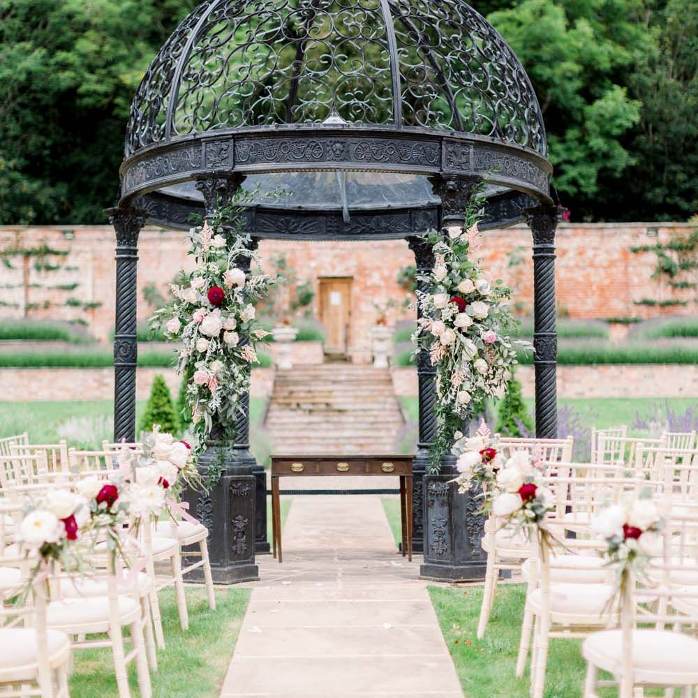 Outdoor alter at Garthmyl Hall with white chairs, a black gazebo and pink floral decorations