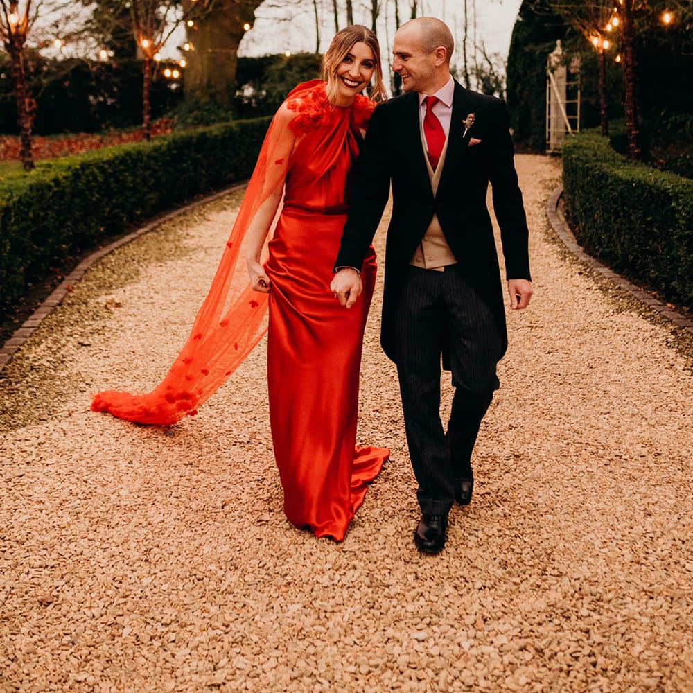 Bride in red silk wedding dress with cape and groom in three piece suit with red tie holding hands
