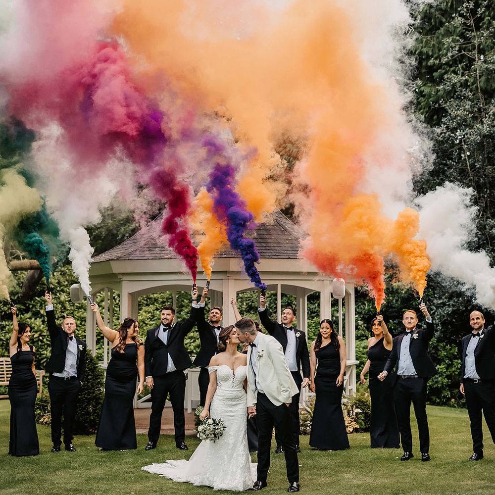 Bride and groom with their wedding party in monochrome black and white outfits let off colourful smoke bombs