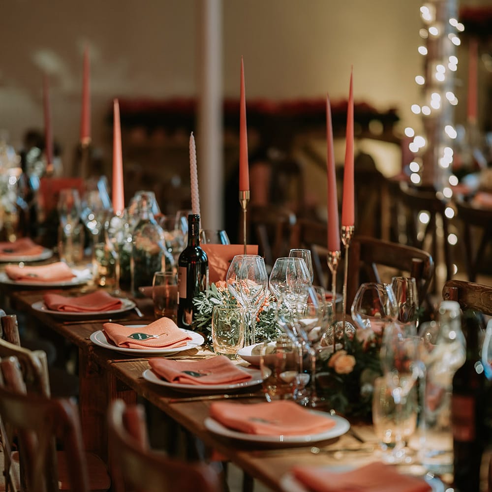 Neutral Christmas wedding tablescape with orange tapered candles, orange napkins, orange rose and foliage tablerunners and fairy lights 
