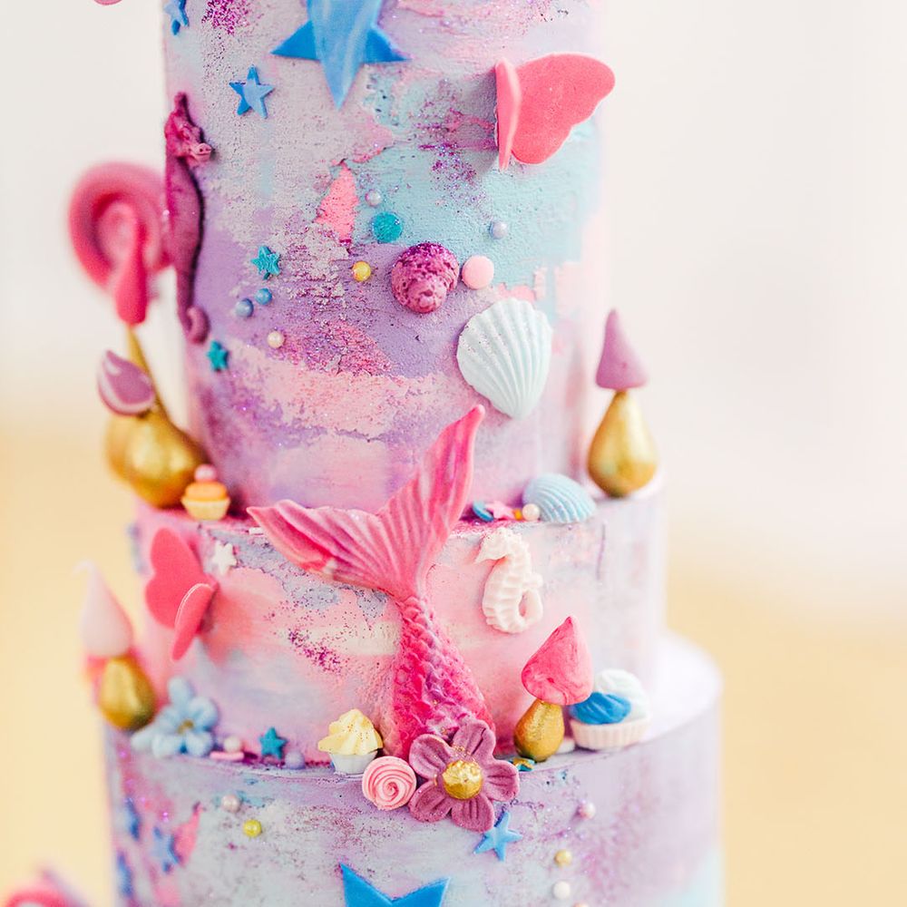 Four tier pink and purple wedding cake with pink mermaid tail, lollipops, stars, butterflies, shells and other small icing details 