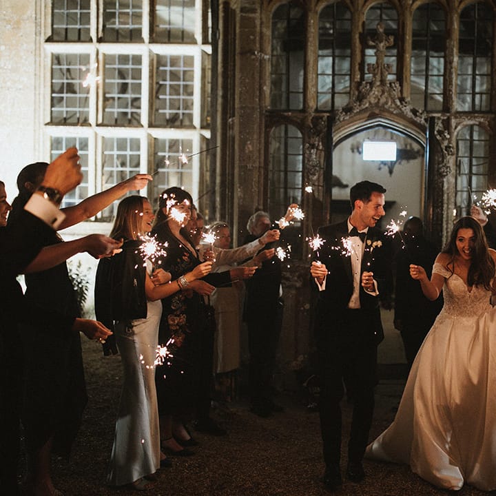 Bride and groom walking together as their wedding guests wave sparklers around 