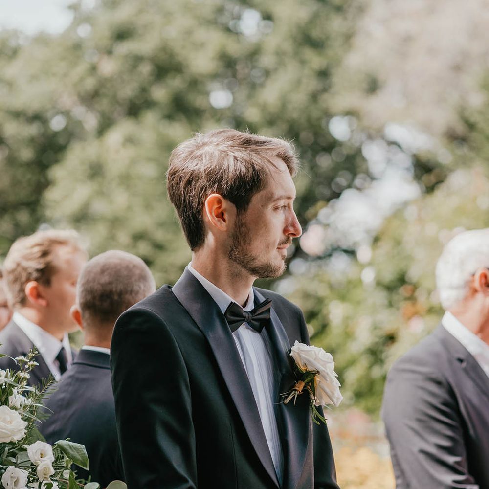 The groom stands at the altar waiting for the bride wearing a blue tuxedo and white rose buttonhole 