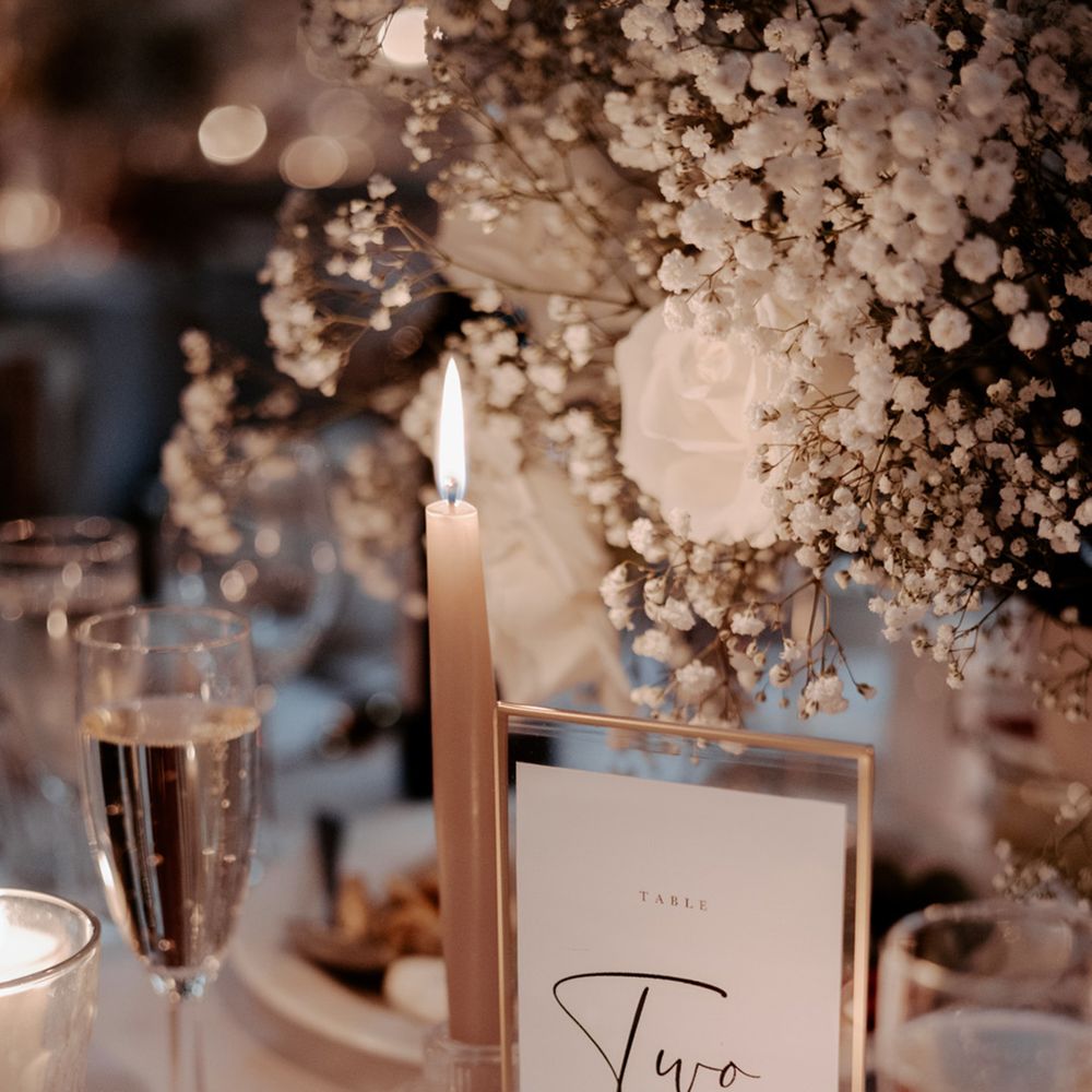 Minimal wedding table sign in gold photo frame with white candle and rose and gypsophila centrepiece 