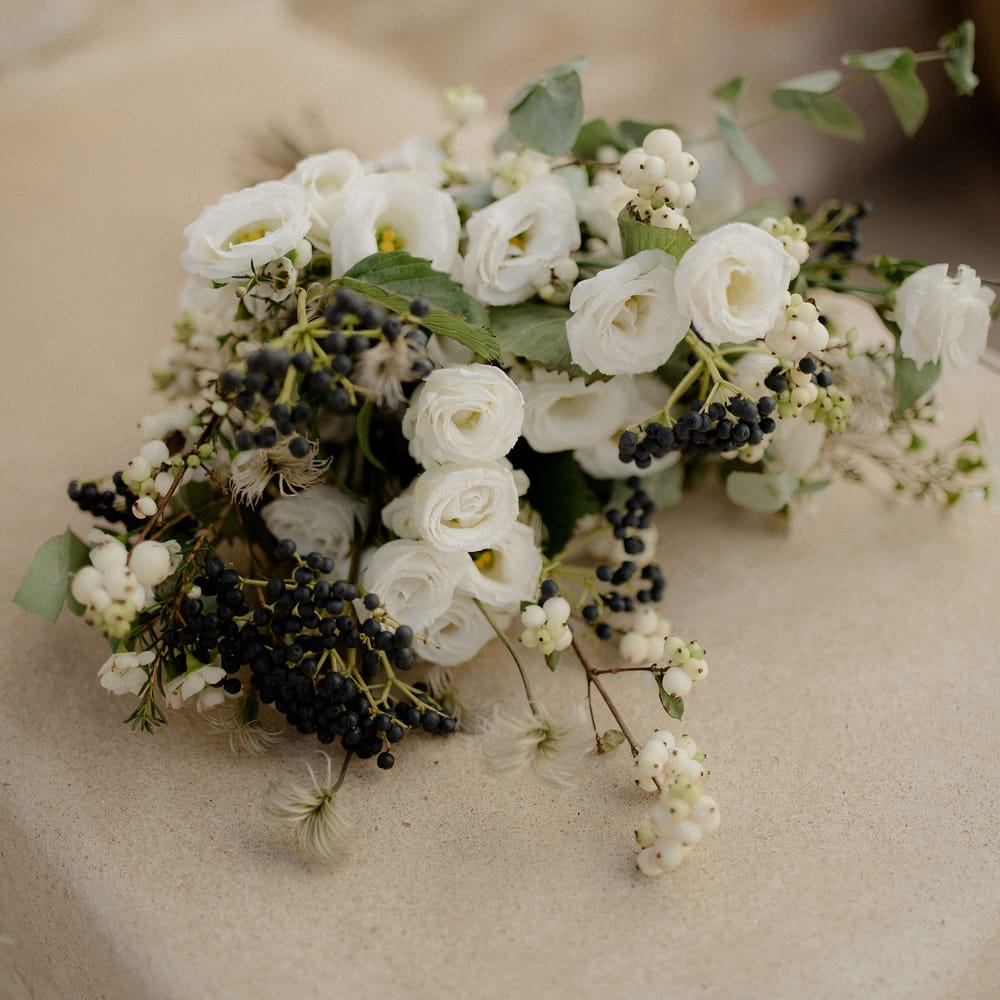 White flower bouquet featuring white roses, white berries, italian ranunculus and eucalyptus