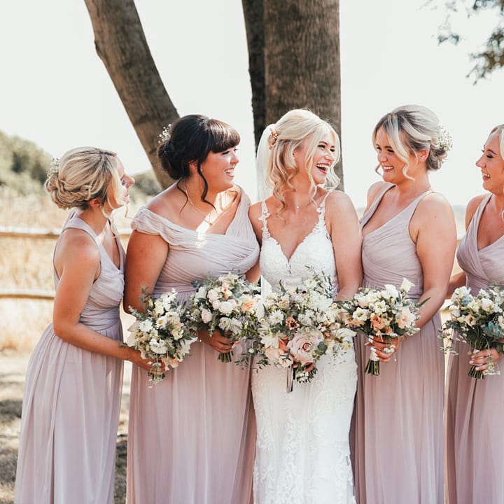 Bridesmaids in pink bridesmaid dresses with the bride in a fitted lace wedding dress with gypsophila in their hair and white bouquets 