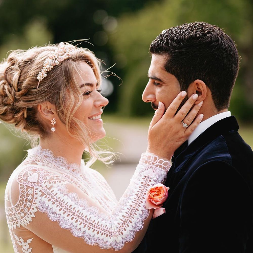 Bride in long sleeve delicate lace wedding dress with pave engagement ring and tiara with the groom in velvet suit jacket 