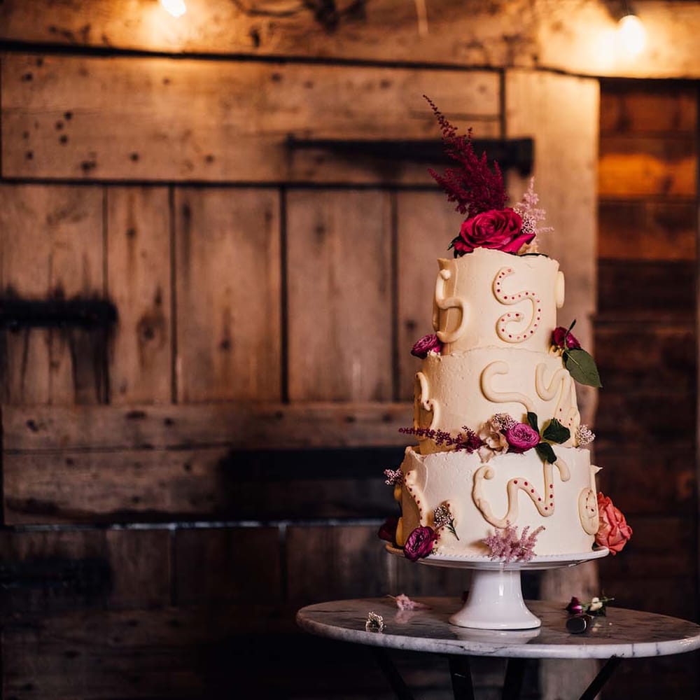Three tier white frosted wedding cake decorated with pink flowers and squiggly icing 