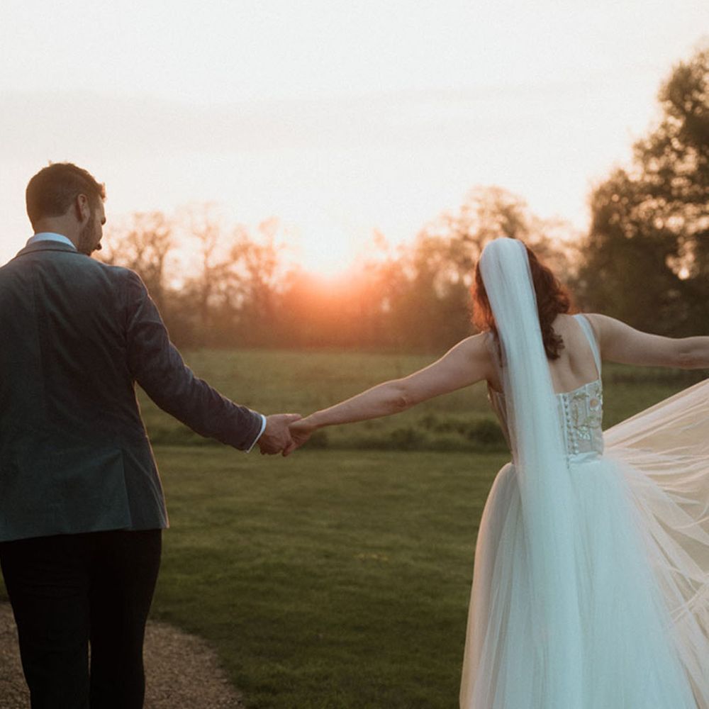 The bride and groom walk hand in hand at golden hour 