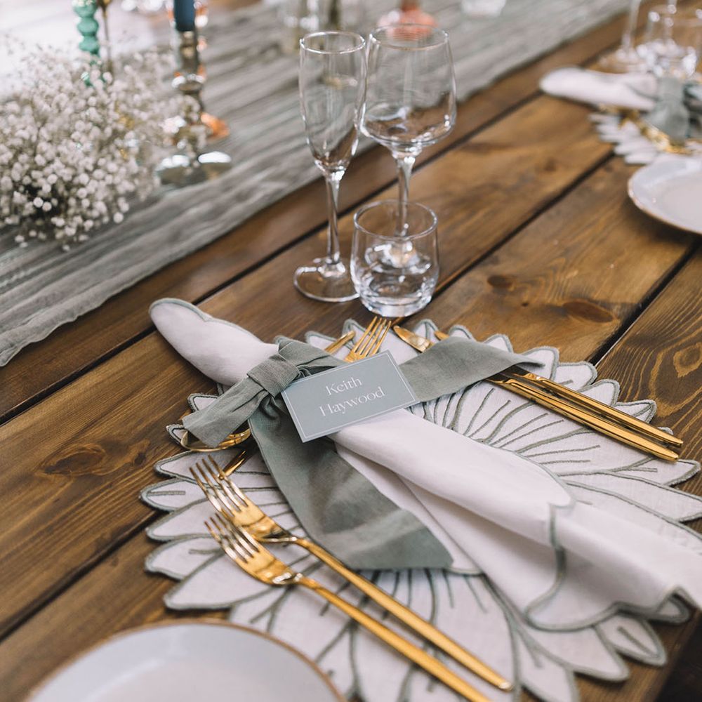 Floral place mats with gold and sage green wedding theme including gold cutlery and pastel candles and bud vases 