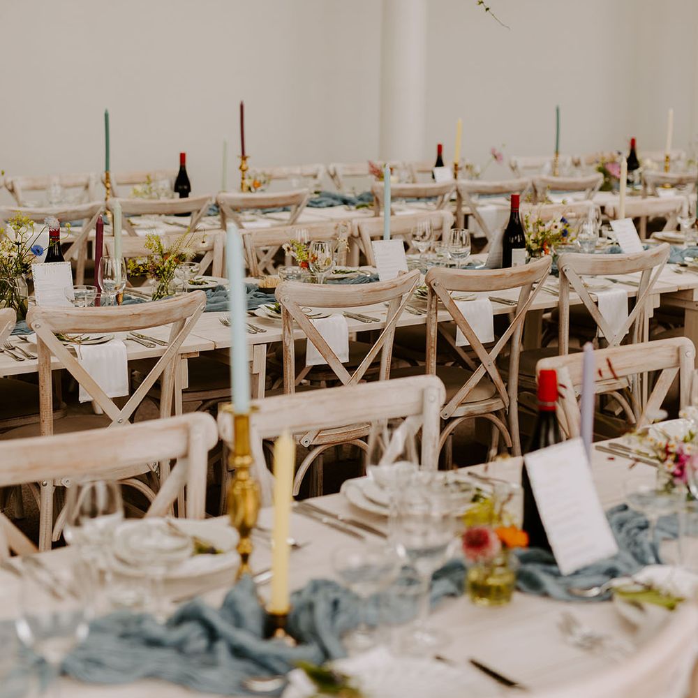 Long banquet tables decorated with dusty blue table runners and pastel wedding candles and decor 