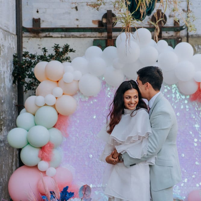 Groom in pale green suit embracing his bride in short wedding dress at holographic pastel festival wedding 