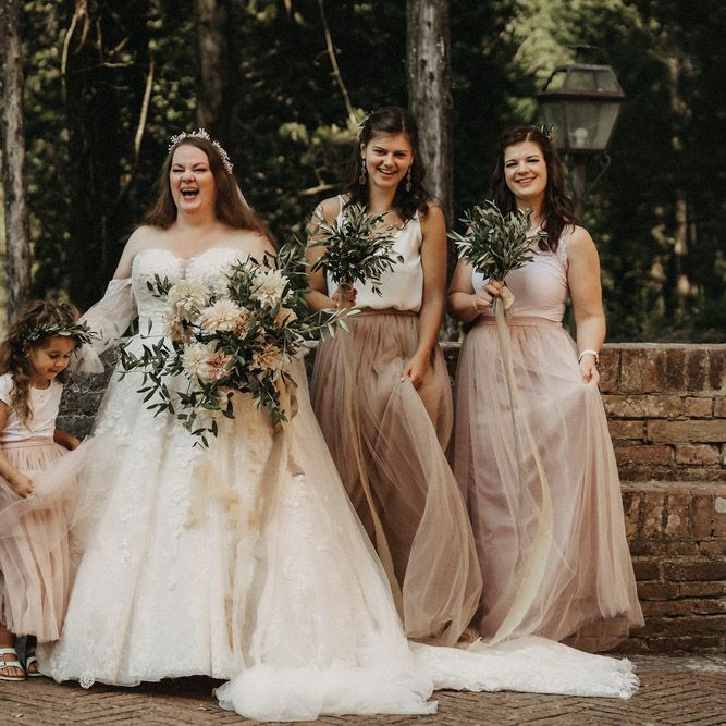 Bridesmaids play with tulle skirts while bride holds olive bouquet