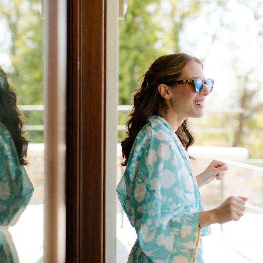 The bride getting ready in the sunshine in a blue dressing gown and sunglasses