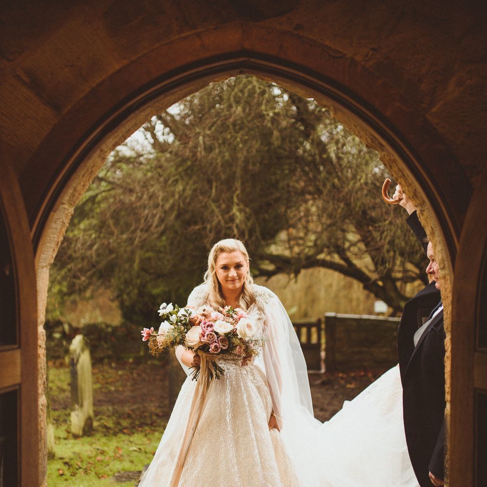 Bride in a princess wedding dress with silver thread holding a blush pink wedding bouquet outside the church 