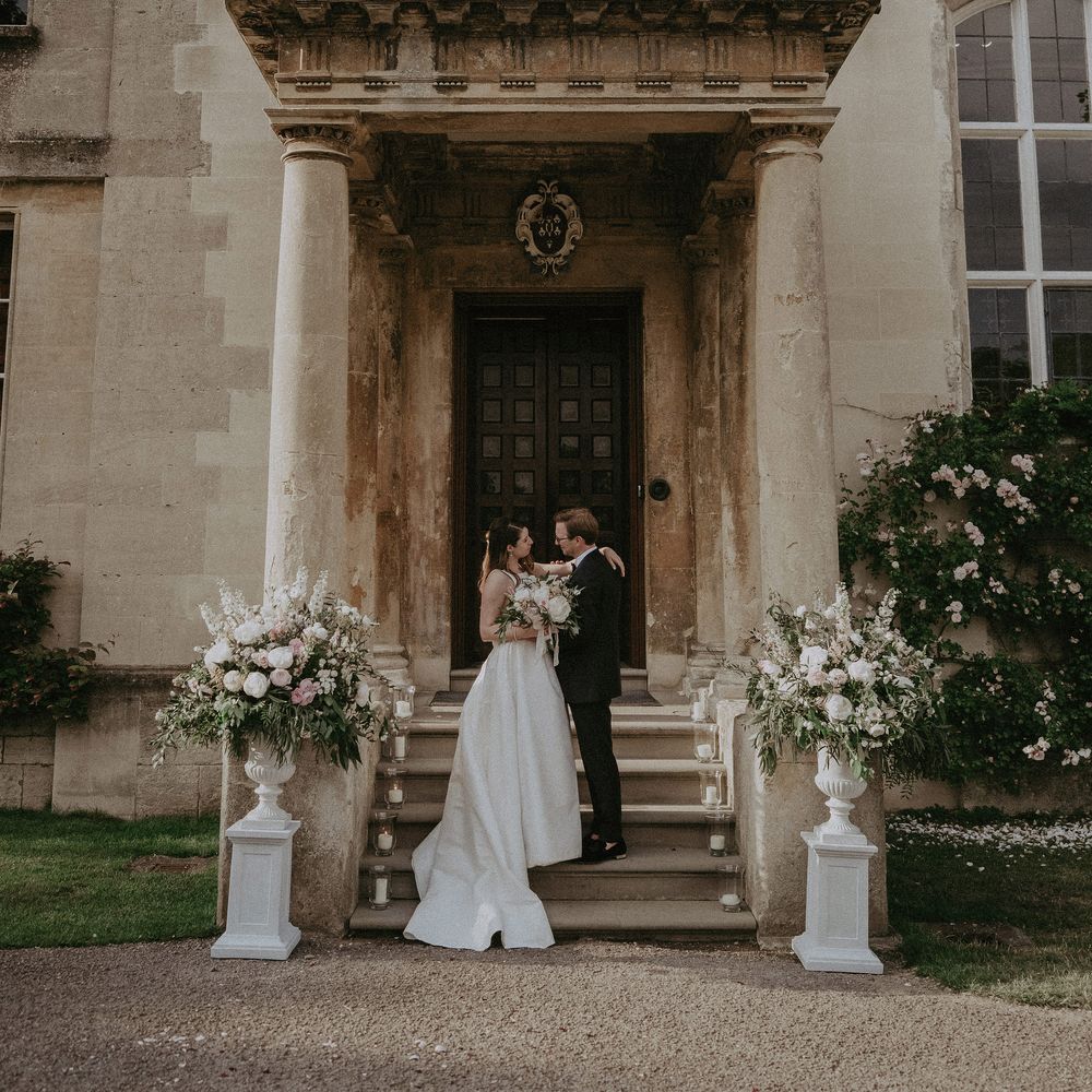 Bride & groom stand in front of large doorway at Elmore court on the day of their wedding