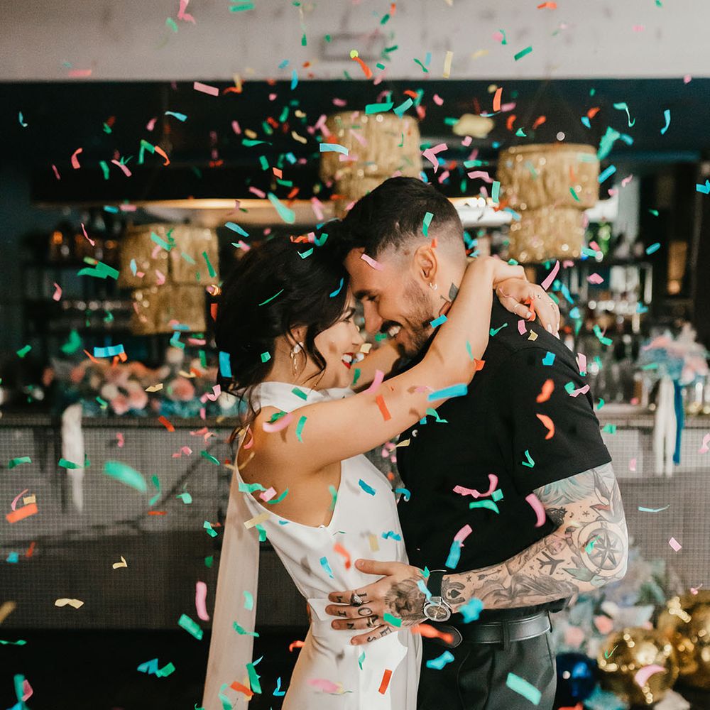 colourful confetti moment with bride in a halterneck wedding dress and red lipstick and groom in a short sleeve black shirt 