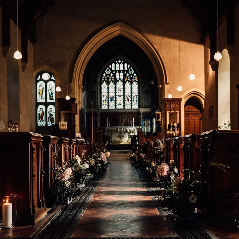 Interior of Cornish church wedding ceremony with florals, candles and hanging lights