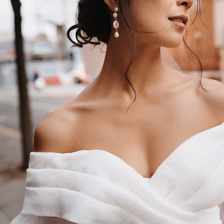 Bride wearing pearl drop earrings and off the shoulder pleated front wedding dress 