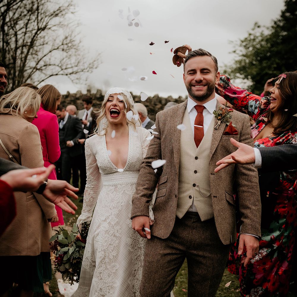 Confetti moment with groom in a brown and beige wool suit and bride in a lace boho wedding dress with Juliet cap veil