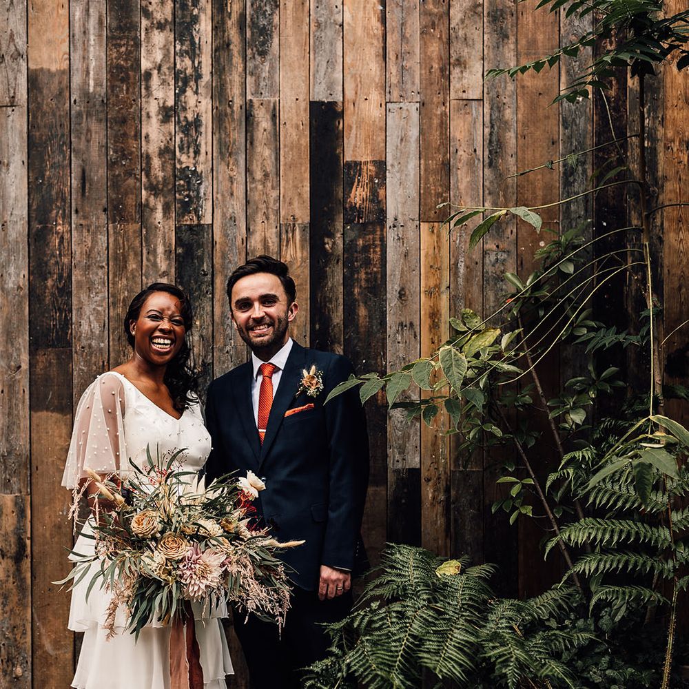 Black bride in a layered skirt and pearl top by Story Of My Dress with her husband in a navy suit at their 100 Barrington wedding in London 