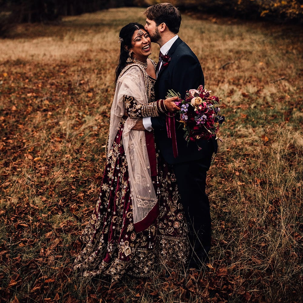 Bride wears Indian Saare wedding dress & holds bouquet of flowers in field with Groom 
