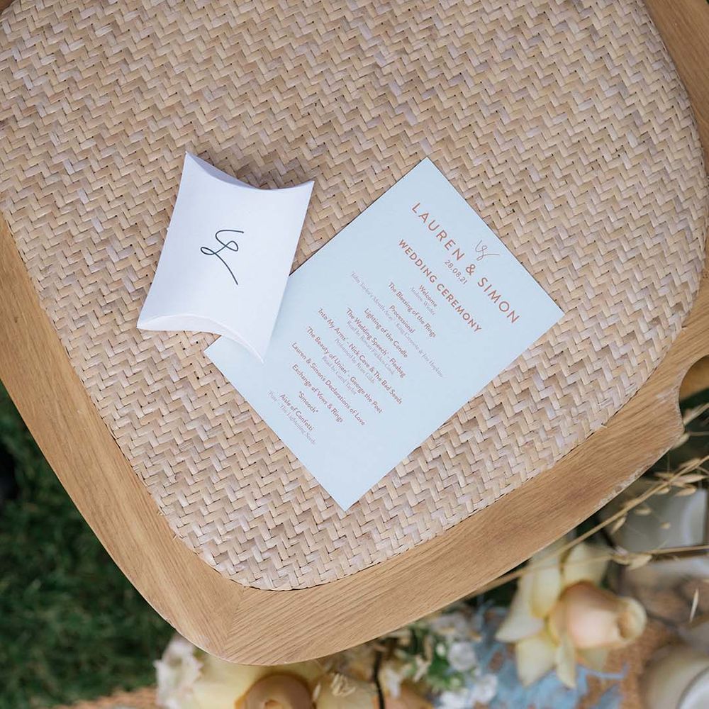 Wedding stationery order of the day card with orange font on wooden chairs for wedding ceremony