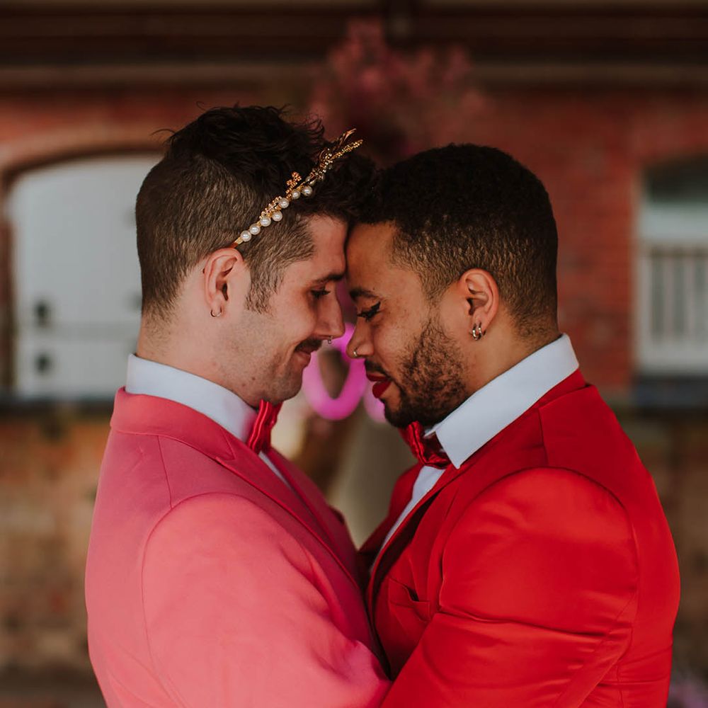 LGBTQI+ couple embracing in pink and red wedding suits 