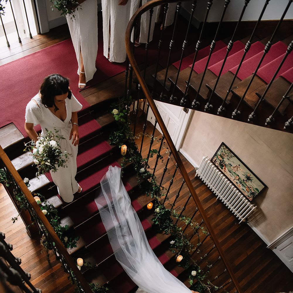 Bridesmaids in sparkly white dresses walk down the stairs behind the bride 