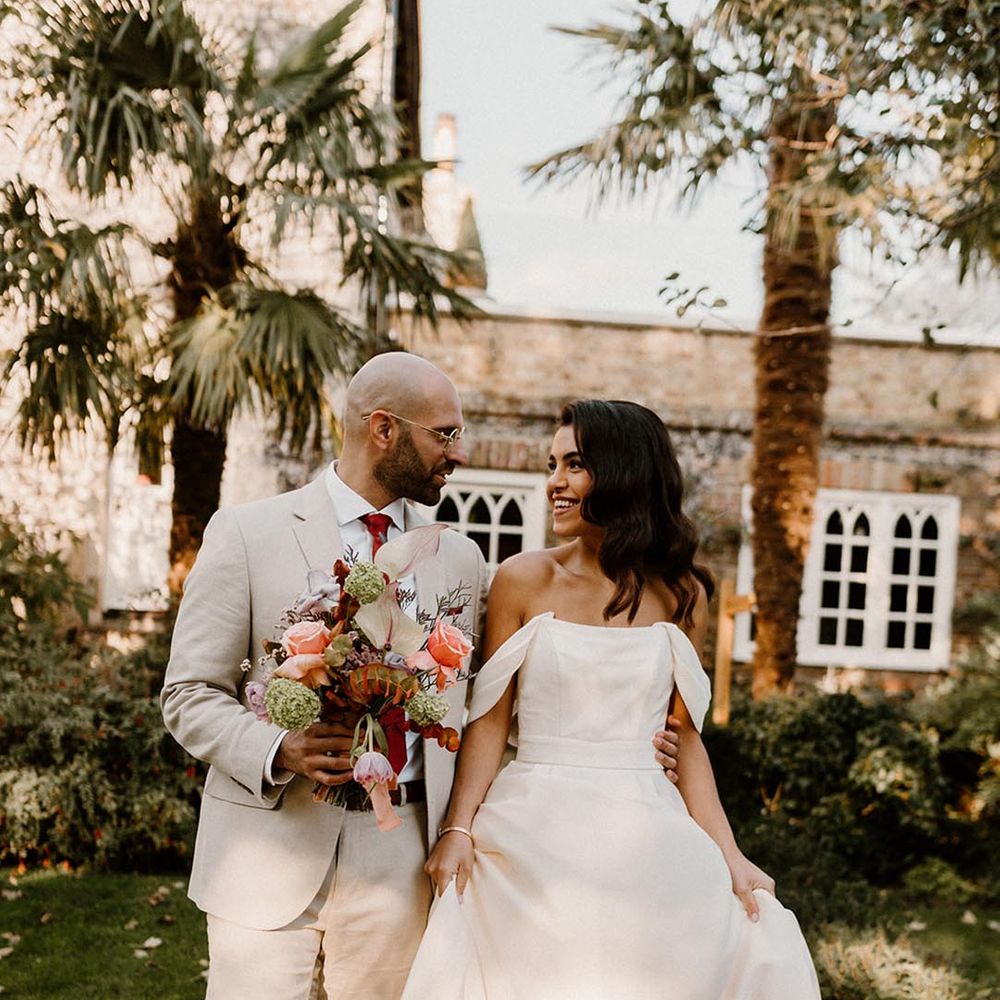 Groom in a pale grey suit with dark red tie and the bride in an off the shoulder wedding dress at the Chapel House Estate
