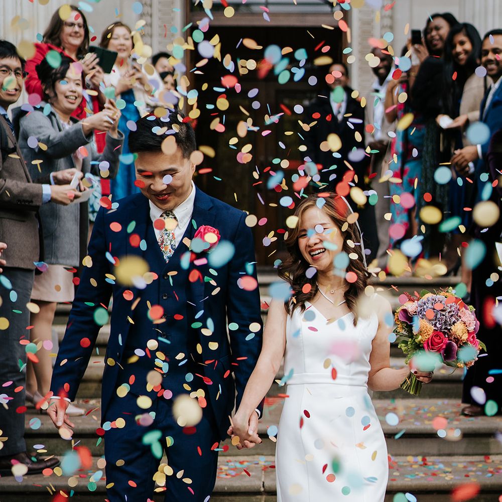 Bride & groom walk through colourful confetti outdoors after wedding ceremony 