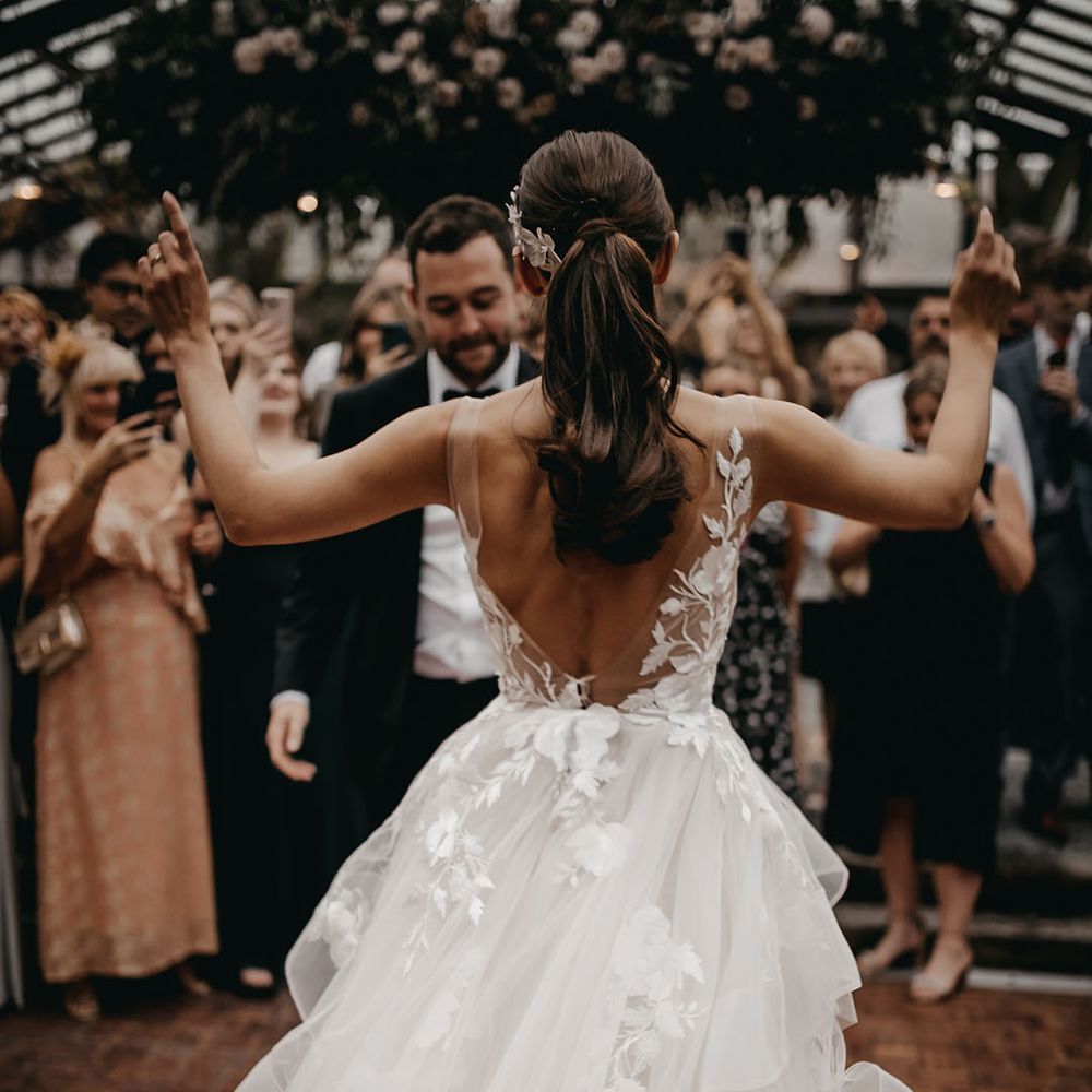 Bride with brown hair in a low pony dances with the groom wearing a low back illusion lace and tulle wedding dress