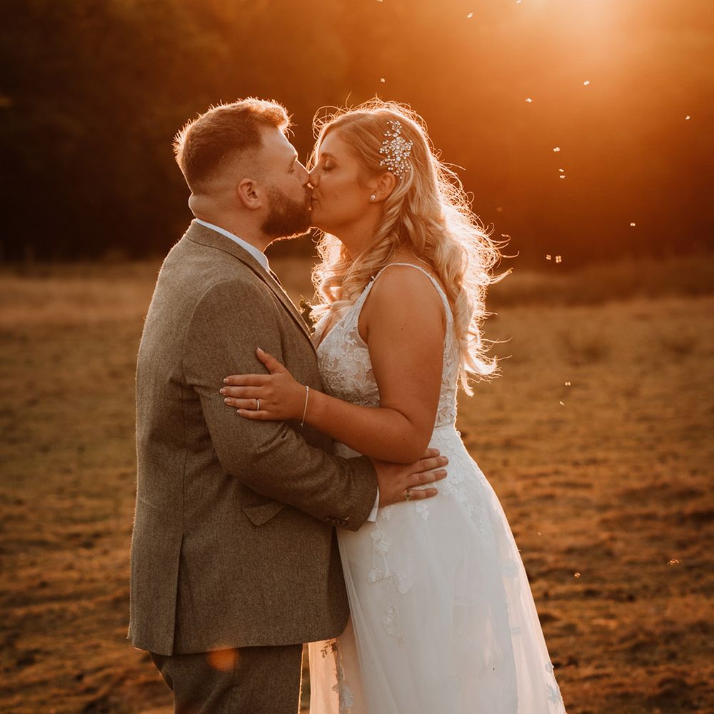 The bride with a sparkly hairpiece kisses the groom during golden hour 