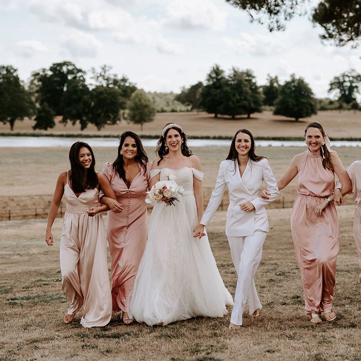 Bridesmaids in pink and champagne dresses with the bride in an off the shoulder wedding dress and bride in white suit 