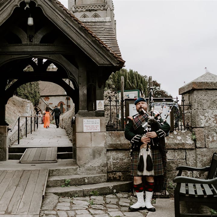 Traditional Scottish bagpipe player stands playing at the entrance to the church 